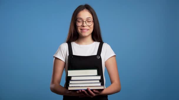 Asiática estudiante sobre fondo azul en el estudio tiene pila de libros universitarios de la biblioteca. Mujer sonríe, ella está feliz de graduarse . — Vídeos de Stock