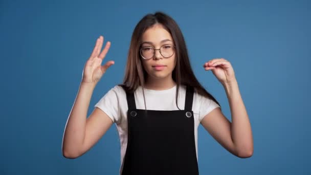 Roztomilá žena v brýlích ukazuje bla-bla-bla gesto s rukama a zvlněné oči izolované na modrém pozadí. Prázdné sliby, blah koncept. Lier. — Stock video