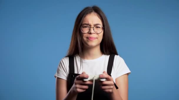 Mooi Aziatisch meisje spelen video spannend spel op TV met joystick op blauwe studio muur. Gebruik van moderne technologie. — Stockvideo