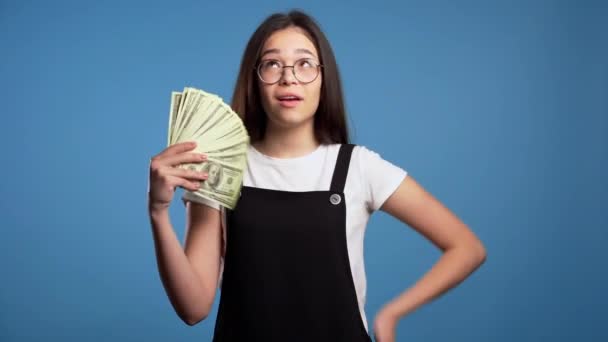 Nöjd glad glad glad asiatisk flicka visar pengar - amerikanska dollar sedlar på blå vägg. Symbol för framgång, vinst, seger. — Stockvideo