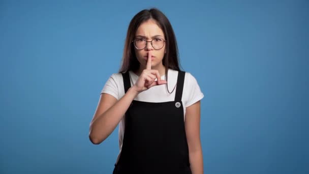 Femme asiatique sérieuse avec les cheveux longs tenant doigt sur ses lèvres sur fond bleu. Un geste de chut, secret, silence. Gros plan . — Video