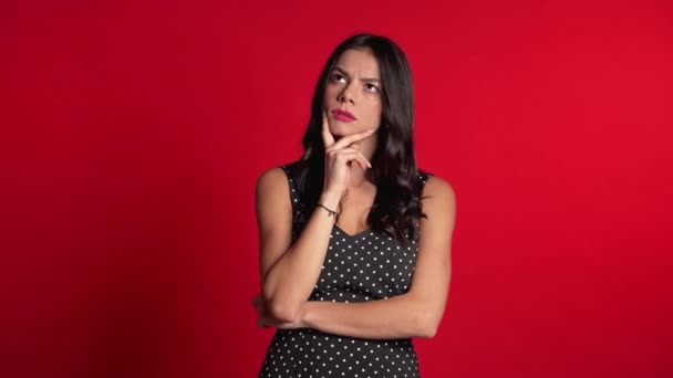 Egy gondolkodó nő, aki vörös háttér után kutat. Aggódó elmélkedő arckifejezések. Csinos latin lány modell — Stock videók