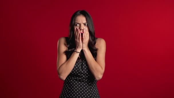 Frightened hispanic woman afraid of something and looks into camera with big eyes full of horror over red wall background. Bad shocking news. — 비디오