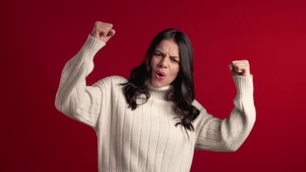 Sorprendido emocionado mujer latina feliz en suéter sobre fondo rojo. Chica con el pelo largo muestra sí gesto de victoria, ella logró el resultado, metas . — Vídeos de Stock