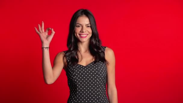 Mladá latinská žena s perfektním make-upem, takže OK podepsat přes červené pozadí. Vítěz. Úspěch. Pozitivní dívka se usmívá do kamery. Jazyk těla. — Stock video
