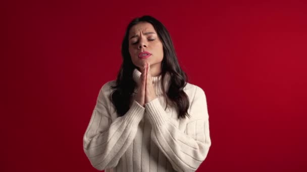 Cute latin young girl in warm white sweater praying over red background. Woman begging someone. 4k. — 비디오