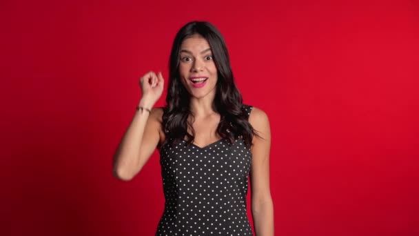 Retrato de una joven hispana pensando en una mujer que tiene un momento de idea apuntando con el dedo hacia arriba en el fondo rojo del estudio. Sonriente chica feliz mostrando gesto eureka . — Vídeos de Stock