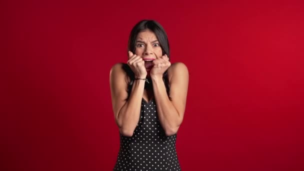 Rädd latinamerikansk kvinna rädd för något och ser in i kameran med stora ögon full av skräck över röd vägg bakgrund. Dåliga chockerande nyheter. — Stockvideo