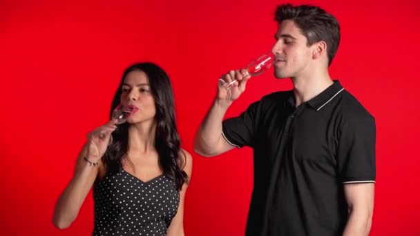 Retrato de una joven pareja bebiendo champán sobre fondo rojo del estudio. Amor, vacaciones, concepto de felicidad . — Vídeo de stock