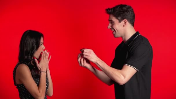Ett ungt par. Mannen friar till sin älskarinna med ring på röd studiobakgrund. Kärlek, semester, lycka koncept. — Stockvideo