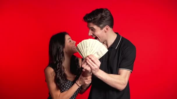 Satisfied happy excited european couple showing money - U.S. currency dollars banknotes on red wall. Symbol of success, gain, victory — 비디오