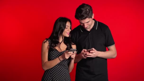 Jeune couple utilisant leurs appareils mobiles et en parler et des applications sur fond de studio rouge — Video