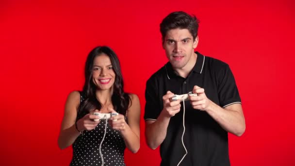 Pareja bastante joven jugando a videojuegos emocionantes en Tv con joystick en la pared del estudio rojo. Uso de tecnología moderna . — Vídeo de stock