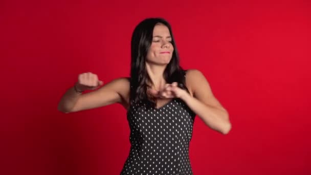 Bastante chica latina en vestido sonriendo y bailando en excelente estado de ánimo sobre fondo rojo. Felicidad, concepto de fiesta . — Vídeos de Stock