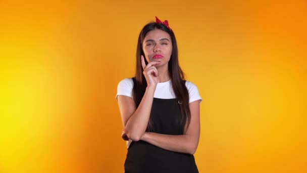 Retrato de una joven pensando en una mujer con un momento de idea apuntando con el dedo hacia arriba en el fondo amarillo del estudio. Sonriente chica feliz mostrando gesto eureka . — Vídeos de Stock