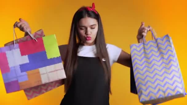 Sarı stüdyo arka planında izole edilmiş alışveriş sonrası renkli kese kağıtlarıyla mutlu genç bir kadın. Mevsimlik satış, alışverişler, hediye konseptine para harcamak. — Stok video