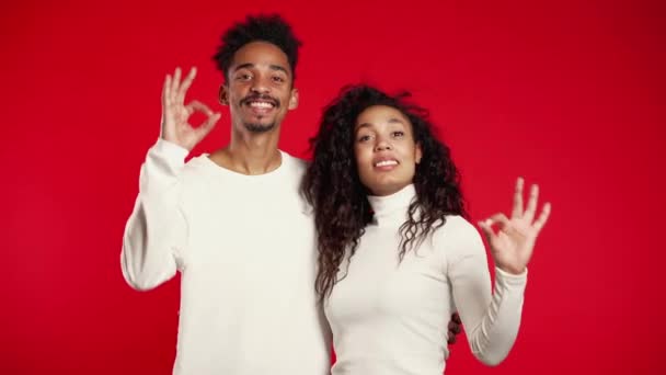 Young african couple making OK sign over red background. Winner. Success. Positive girl and man smiles to camera. Body language. — 비디오