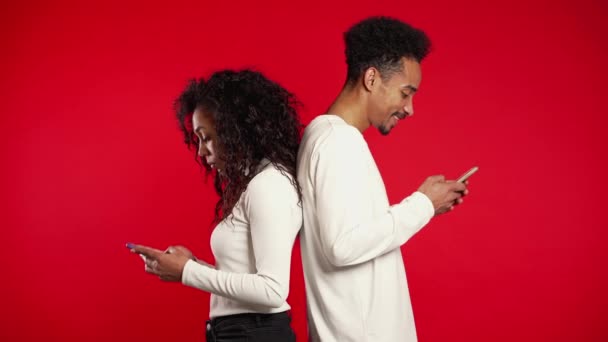 Couple stand with their backs to each other, printing messages or surf Internet. Woman is peeking over her boyfriends shoulder, while he is communicating via mobile telephone. Trick concept. — 비디오