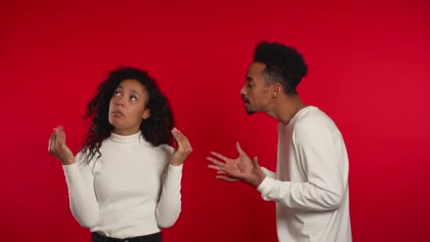 African woman showing bla-bla-bla gesture with hands and rolling eyes while boyfriend trying to say something. Couple isolated on red background. Empty promises, blah concept. Lier. — Stockvideo
