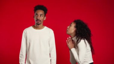 Cute african young woman begging her boyfriend or husband about something over red background. 