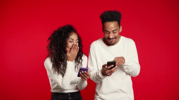 Young couple using their mobile devices, laughing and talking about it. Social apps on red studio background — 비디오