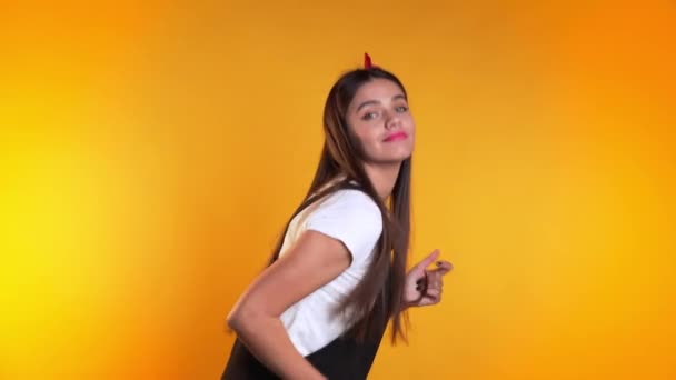 Pretty young girl in dress smiling and dancing in excellent mood on yellow background. Happiness, party concept. — Stok video