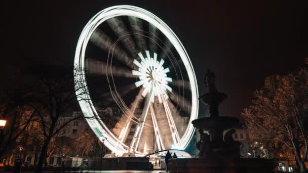 Timelapse of brightly lit ferris wheel ride, which spinning at night or evening carnival. Low angle. Colored lights flashing. Concept of amusement park, fair, thrill. Budapest eye, Hungary. — Stockvideo