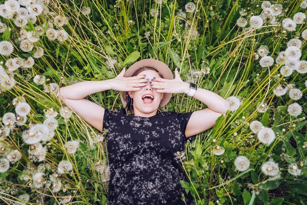 Giovane bella ragazza in occhiali da sole si trova nel campo di dente di leone e chiudere gli occhi con gioia. Vista dall'alto . — Foto Stock