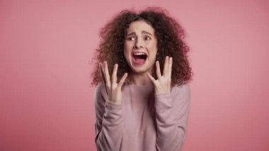 Close up of young scared curly girl shouting isolated over pink background. Stressed and depressed woman 4k