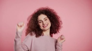 Pembe stüdyo arka planında kıvırcık saçlı güzel bir kadın dans ediyor. Şirin kızlar portresi. Parti, mutluluk, özgürlük, gençlik kavramı.