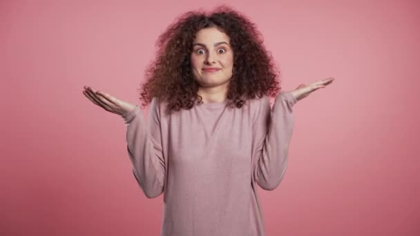 Jeune fille bouclée incertaine hausse les bras, fait un geste de je ne sais pas, soins, ne peut rien aider. Jeune femme bouclée avec des taches de rousseur paillettes à la mode maquillage — Video