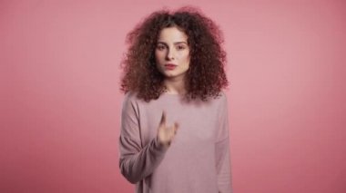 Pembe arka planda parmaklarını dudaklarında tutan pozitif kız. Şşş, sır, sessizlik jesti. Kapatın. Vücut dili. Parlak çilli, genç kıvırcık kadın makyaj yapıyor.
