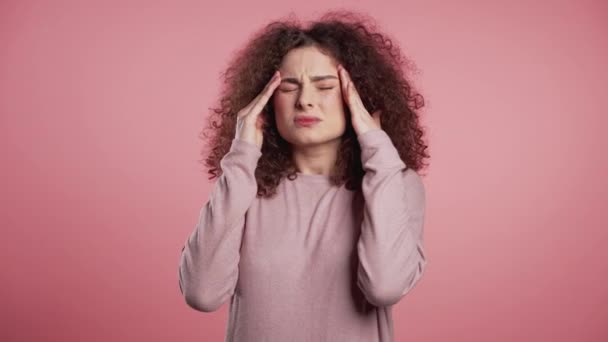 Joven hermosa mujer con el pelo rizado con dolor de cabeza, retrato de estudio rosa. Chica poniendo las manos en la cabeza, aislado en el fondo. Concepto de problemas y dolor de cabeza . — Vídeo de stock