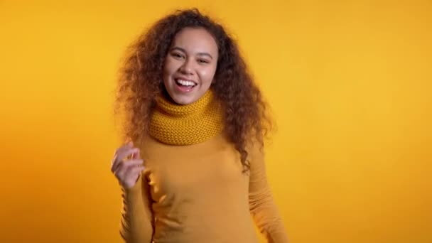 Mooie vrouw met krullend haar dansend met handen op gele studio achtergrond. Schattig meisjes portret. Feest, geluk, vrijheid, jeugdconcept. — Stockvideo