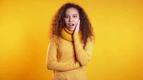 Positive girl holding finger on her lips over yellow background. Gesture of shhh, secret, silence. Close up. Body language. Young curly woman — Stock Video
