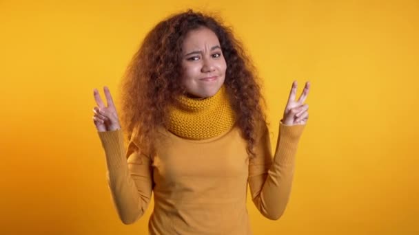 Ładna kręcona dziewczyna pokazuje z rękami i dwoma palcami jak cytaty gest, zginać palce izolowane na żółtym tle. Bardzo zabawna, ironiczna i sarkastyczna koncepcja. — Wideo stockowe