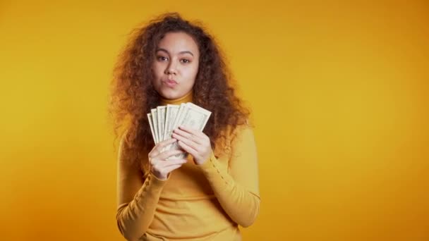 Spokojeně nadšená dívka ukazující peníze - bankovky v amerických měnách na žluté stěně. Symbol úspěchu, zisku, vítězství. — Stock video