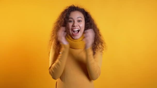 Girl with curly hair very glad and happy, she shows yes gesture of victory, she achieved result, goals. Surprised excited happy woman on yellow background — Stock Video