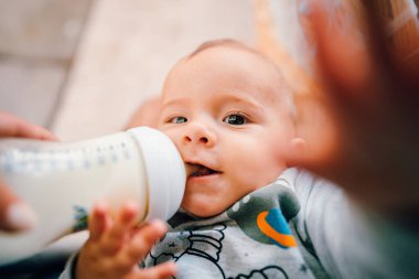 Little baby boy drinking mother milk from the bottle and smiling
