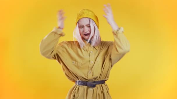 Pembe saçlı, stüdyo portresi olan üzgün genç bir kadın. Kız ellerini başının üstüne koyuyor, sarı arka planda izole edilmiş. Sıkıntı ve sorun kavramı — Stok video