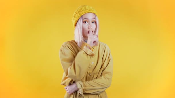 一个积极的女孩在黄色的背景上用手指捂住嘴唇.嘘的手势，秘密，沉默。靠近点身体语言。年轻的朋克女人 — 图库视频影像