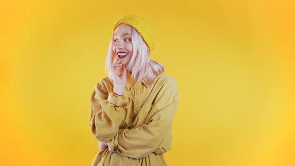 Hezká mladá dívka s bílými vlasy stojí na žlutém pozadí studia, usmívá se a flirtuje. Roztomilý portrét neobvyklé ženy s piercing — Stock video
