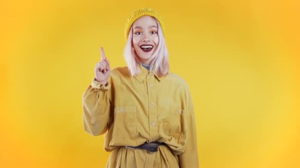 Porträt einer nachdenklichen jungen Frau, die auf gelbem Studiohintergrund mit erhobenem Zeigefinger eine Idee hat. lächelndes glückliches Mädchen zeigt Eureka-Geste. — Stockvideo