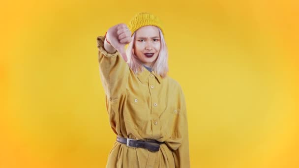 Young pretty woman standing on yellow studio background expressing discontent and showing thumb down gesture at camera. Portrait of girl with sign of dislike — Stock Video