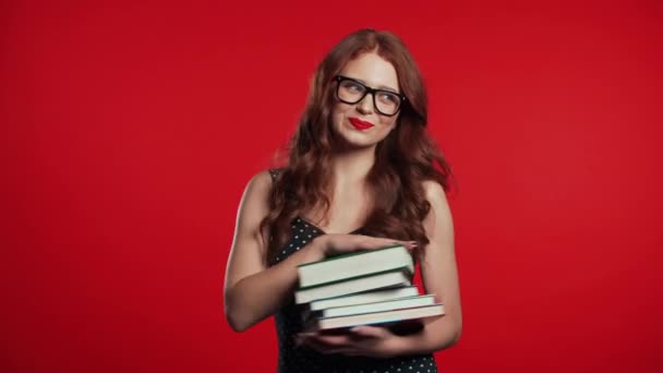 Estudiante europeo sobre fondo rojo en el estudio tiene pila de libros universitarios de la biblioteca. Mujer sonríe, ella está feliz de graduarse . — Vídeos de Stock