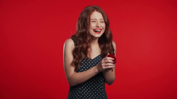 Mujer joven bastante europea en vestido sosteniendo pequeña caja de joyería con anillo de diamantes propuesta sobre fondo de pared roja. Chica sonriendo, ella está feliz de estar presente, proposición para el matrimonio . — Vídeos de Stock