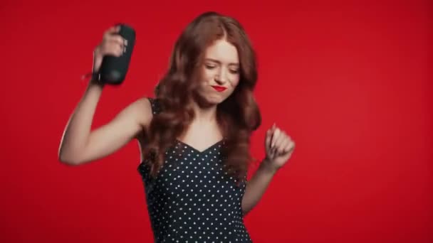 Trendig tjej lyssnar på musik med trådlös bärbar högtalare. Ung vacker kvinna med röd frisyr njuter och dansa på studio bakgrund. Kvinnliga flyttar till rytmen av musik. — Stockvideo