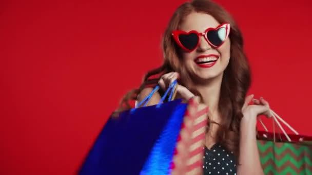 Feliz mujer joven de estilo retro con el pelo rojo y bolsas de papel después de comprar aislado en el fondo del estudio. Venta estacional, compras, gasto en concepto de regalos — Vídeo de stock