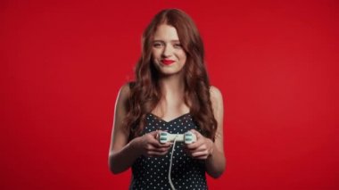 Pretty young girl playing video exciting game on Tv with joystick on red studio wall. Using modern technology. 