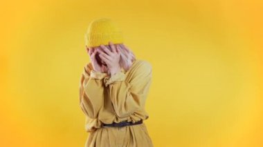 Kıvırcık saçlı, başı ağrıyan, stüdyo portresi olan genç üzgün bir kadın. Kız ellerini başının üstüne koyuyor, sarı arka planda izole edilmiş. Sorunlar ve baş ağrısı kavramı.